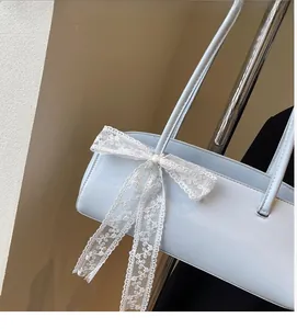 Detail der hellblauen Baguette-Tasche mit einer großen weißen Spitzen-Blumenschleife