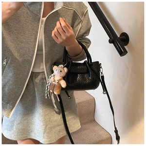 Détail du sac à main noir tressé avec un pendentif ours en peluche et une bandoulière réglable