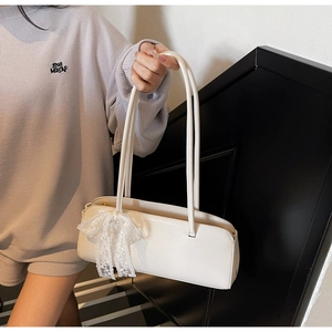 Detail of off-white pillow bag with lace bow pendant held by model on a staircase