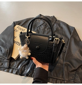 Detail der schwarzen Handtasche mit Krokoprägung, Plüschanhänger und Gurt