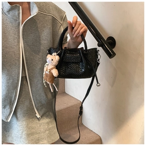 Détail macro du sac seau noir tressé avec un joli pendentif ours en peluche blanc