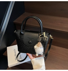 Detailansicht der schwarzen gewebten Handtasche mit Henkel und Plüsch-Anhänger auf Holz