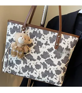 Close-up of cow print tote bag with brown handles and a cute bear charm accessory