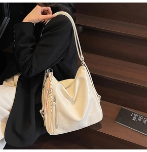 Borsa tote crema lucida con zip argentate e ciondolo arancione su scale in legno scuro