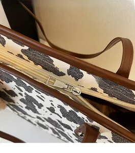 Detail of silver zipper and brown leather trim on a cow print shoulder bag