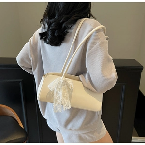 Detail of cream rectangle underarm bag with decorative white lace bow and slim straps