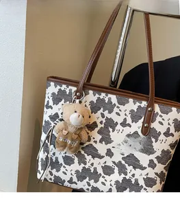 Detail of cow print tote bag featuring brown leather straps and cute plush bear charm