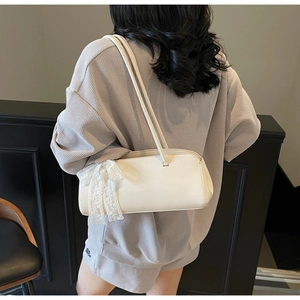 Detail of white rectangular leather underarm bag with decorative lace bow on strap