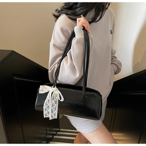 Close-up of black rectangular shoulder bag with large white lace bow detail on strap