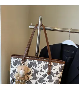 Detail of cow print tote bag featuring brown leather straps and a plush bear charm