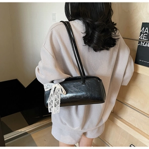 Detail of black glossy shoulder bag featuring delicate white lace bow on the side
