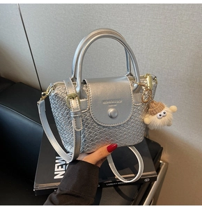 Détail d'un sac à main tissé argenté avec texture métallique et charm boule en peluche
