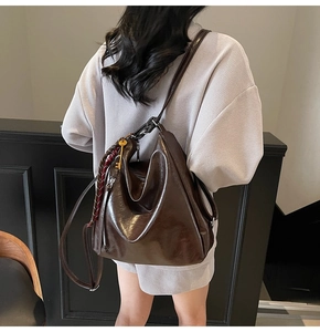 Dettaglio dello zaino hobo in pelle marrone lucida con ciondolo vintage e nastro