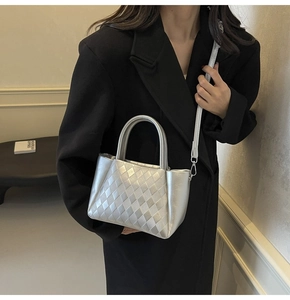 Close-up of silver woven handbag with metallic texture and crossbody strap on black blazer