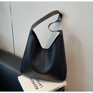 Gros plan d'un grand sac cabas noir minimaliste en cuir mat posé sur un livre blanc