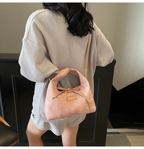 Detail showing pink suede dumpling bag with bow drawstring and gold metal strap buckles