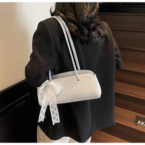 Detail of grey rectangular shoulder bag featuring elegant white lace bow charm and slim straps