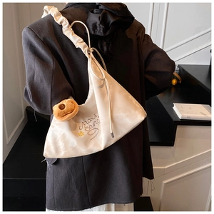 Dettaglio della tracolla a pieghe e borsa beige con simpatico ciondolo a forma di orso