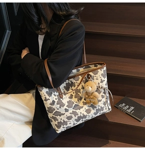 Detail of cow print tote bag with brown leather handles and bear pendant on a model