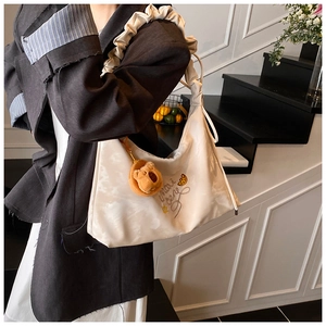 Dettaglio borsa beige con tracolla a pieghe, ricamo e ciondolo a forma di orso