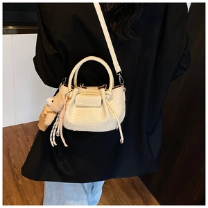 Détail du sac seau tressé crème avec pendentif ours porté sur un blazer noir