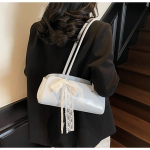 Detail of light blue shoulder bag featuring a large white lace bow and dual handles