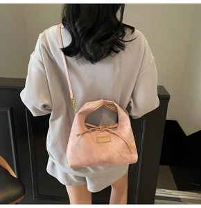 Detailed view of pink dumpling handbag worn crossbody against a grey casual outfit
