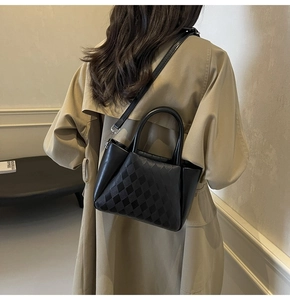 Detail of black checkered embossed leather bucket bag held by a model in a trench coat