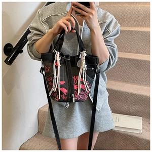 Close-up of black bucket bag featuring graffiti prints, woven ropes, and racquet charms