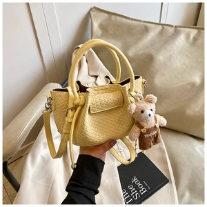 Détail d'un sac seau tressé jaune avec un charm d'ours mignon et des poignées supérieures