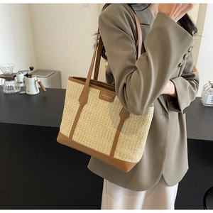 Detail of woven straw tote bag with brown leather handles and fashion logo tag