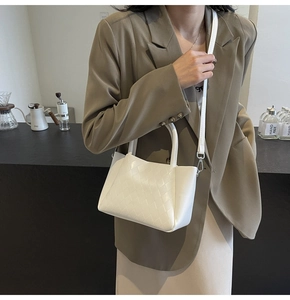 White woven bucket bag with dual handles and crossbody strap styled on a model