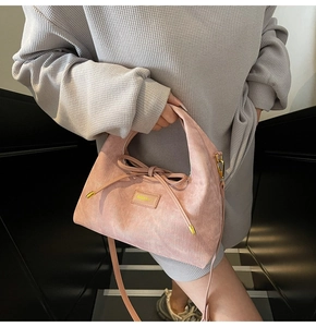 Close-up of pink suede dumpling bag with bow drawstring and adjustable shoulder strap