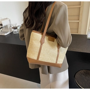 Detail of hand-woven straw tote with brown leather straps shown on shoulder