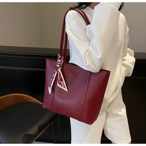 Detail der weinroten Shopper-Tasche mit goldenem Logo und dekorativem Blumenschal
