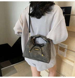 Detail of grey crossbody bag with black ribbon bow and gold HAMIROO brand logo plaque