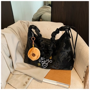 Dettaglio borsa hobo nera con manico a pieghe e ciondolo in peluche su sedia beige