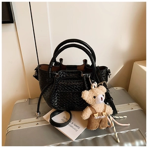 Détail d'un mini sac seau tressé noir avec un petit ours en peluche sur une valise