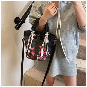 Detail of black denim tote with pink graffiti, long tassels and adjustable strap
