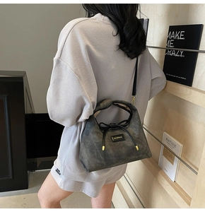 Detail view of a gray suede dumpling bag with black bow and gold brand plaque on model