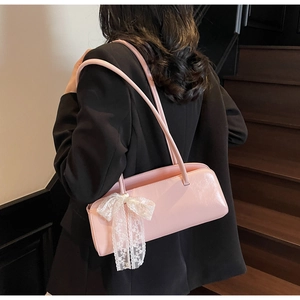 Pink glossy patent leather underarm bag with lace bow accessory on a model's shoulder