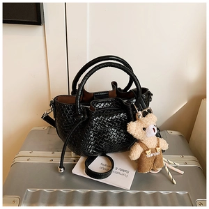 Détail du sac à main noir tressé avec plis ondulés et breloque ours en peluche