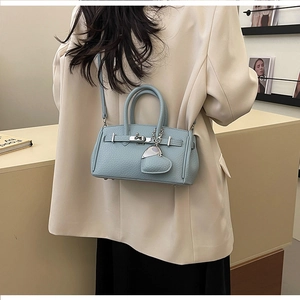 Borsa a mano in pelle azzurra con ciondolo a cuore, indossata a tracolla su una modella
