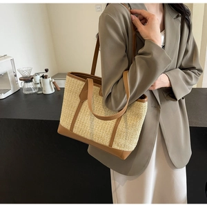 Detail of woven straw tote bag with brown leather handles worn by a model in interior