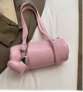 Pink cylinder boston bag with adjustable straps and heart charm on white fabric