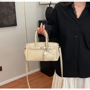 Dettaglio della borsa beige in pelle martellata con chiusura a scatto e ciondolo a cuore