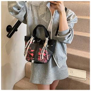 Detail of black denim bucket bag with pink graffiti patterns and white rope tassels