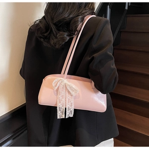Pink glossy pillow bag with white lace bow detail shown on a model's shoulder