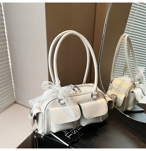 Detail view of cream Boston bag featuring shiny finish, metal buckles and lace bow decoration