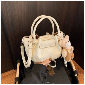Détail du sac seau plissé crème avec texture tressée et breloque ours en peluche